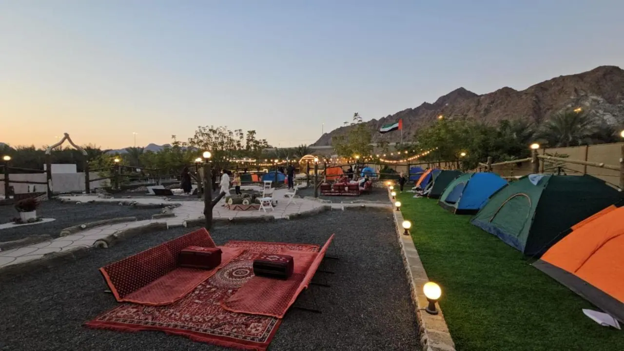 Dafta Valley at sunset, with outdoor majlis seating and camping tents below the mountains